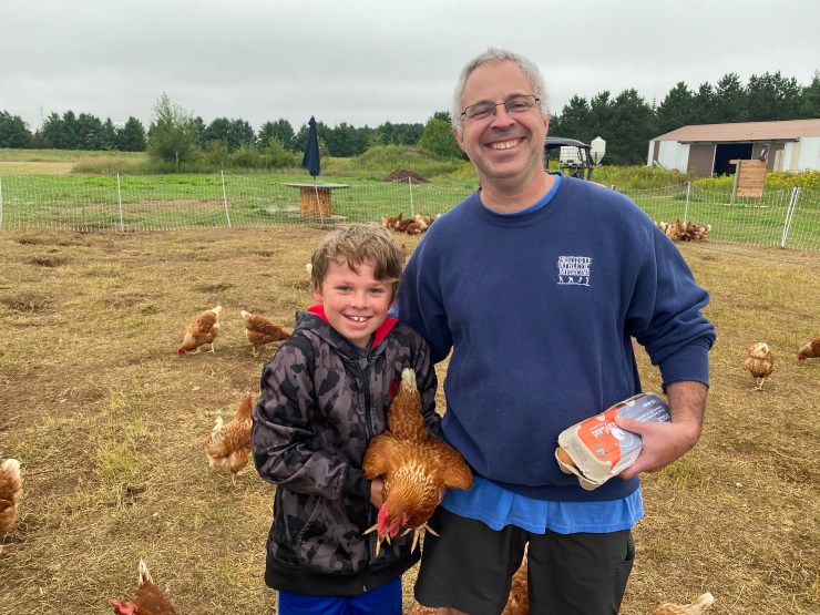 Klay Jaeger and his 9-year-old son, Issac, smile for the camera, holding a chicken and some eggs.