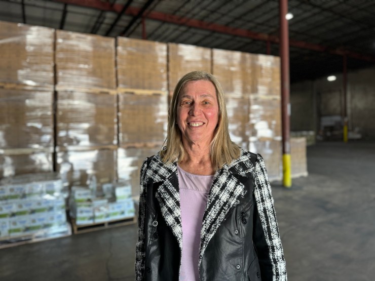 Sue Monaghan smiles in front of pallets in the warehouse.