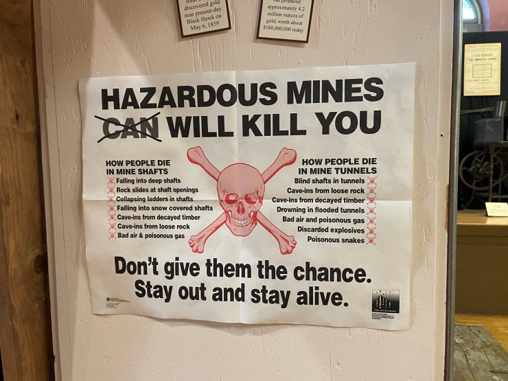 A sign that says "Hazardous mines will kill you" and lists ways people die in mine shafts and tunnels.