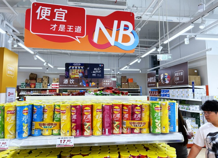 Una unidad de supermercado Alibaba Freshippo en Shanghái muestra un cartel que dice "Lo barato es el rey" sobre tubos de patatas fritas.