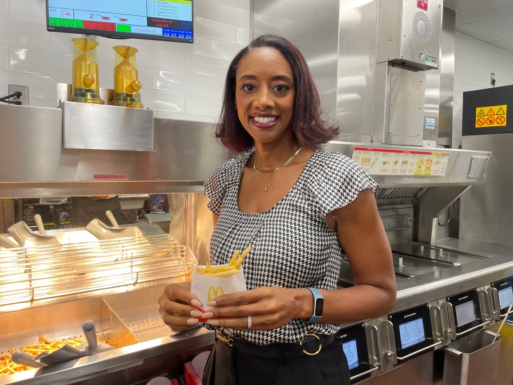 A dark-skinned woman smiles with a small bag of fries from McDonald's.