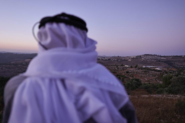 A man wearing a keffiyeh looks out at an Israeli settler outpost.