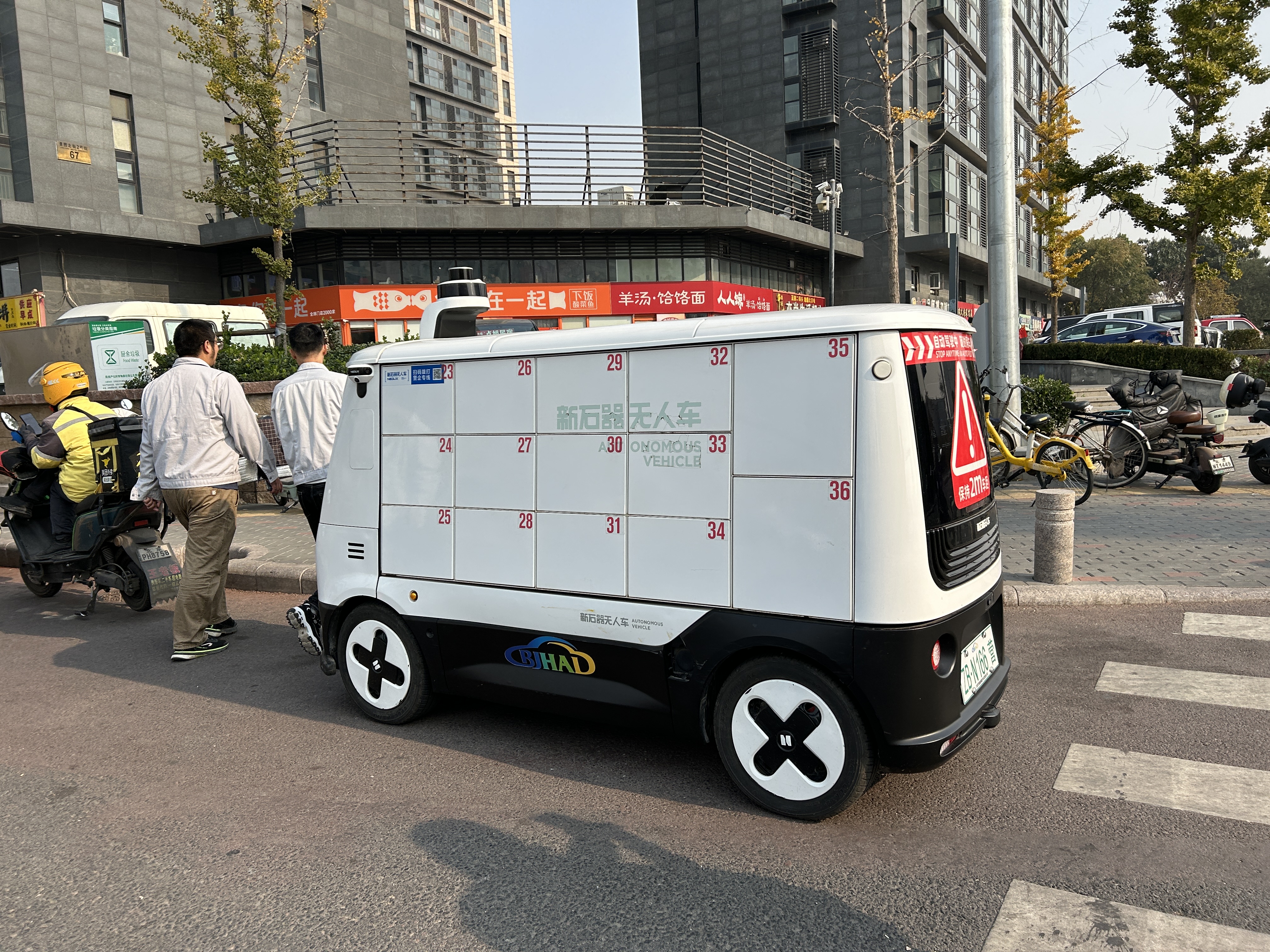 A small white van equipped with sensors parks at the top of a sidewalk. The van has several small numbered doors on the side. 