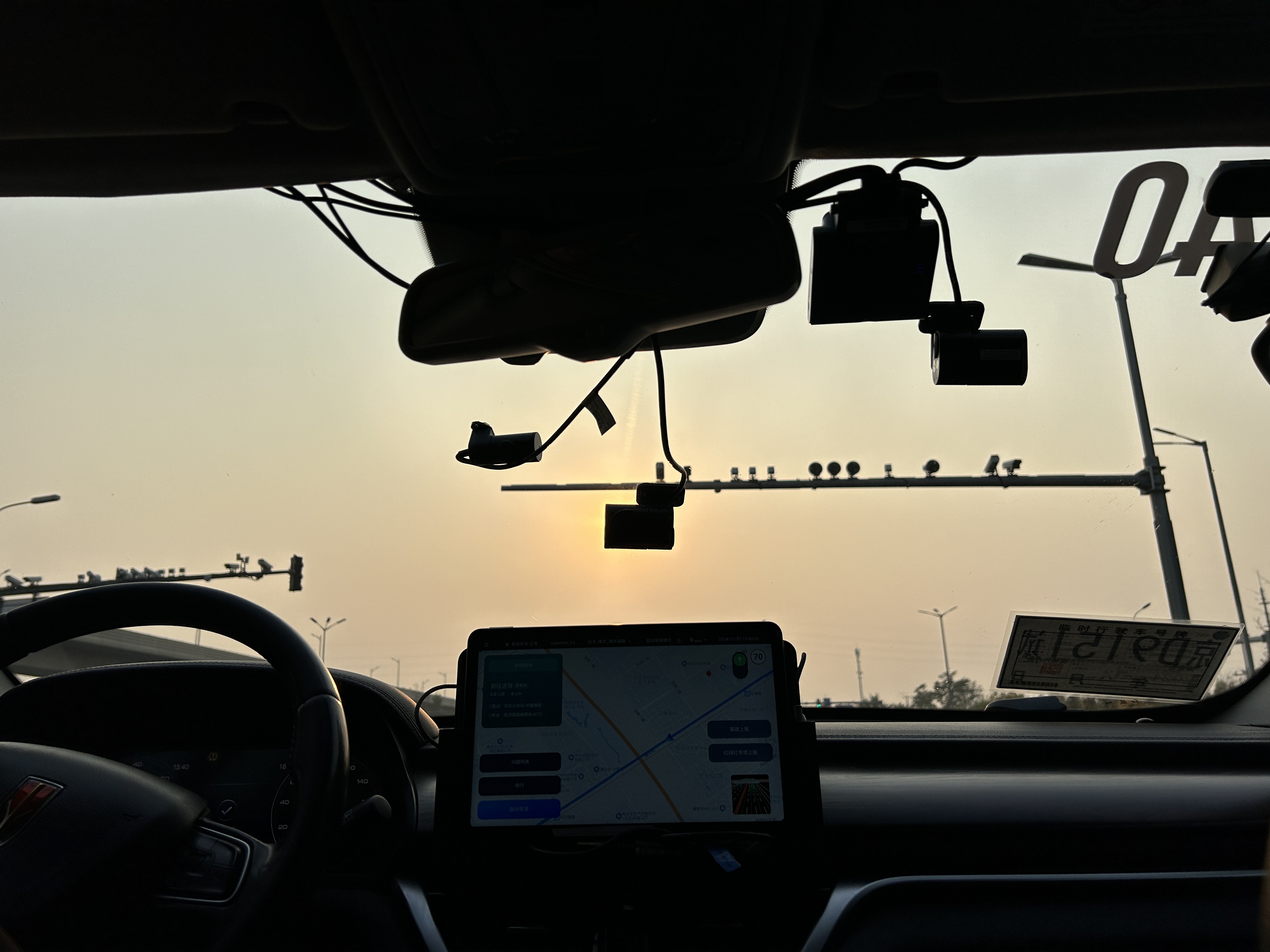 Several cameras perched on horizontal lamp posts stand out against the sun in a photo taken from inside a self-driving car.