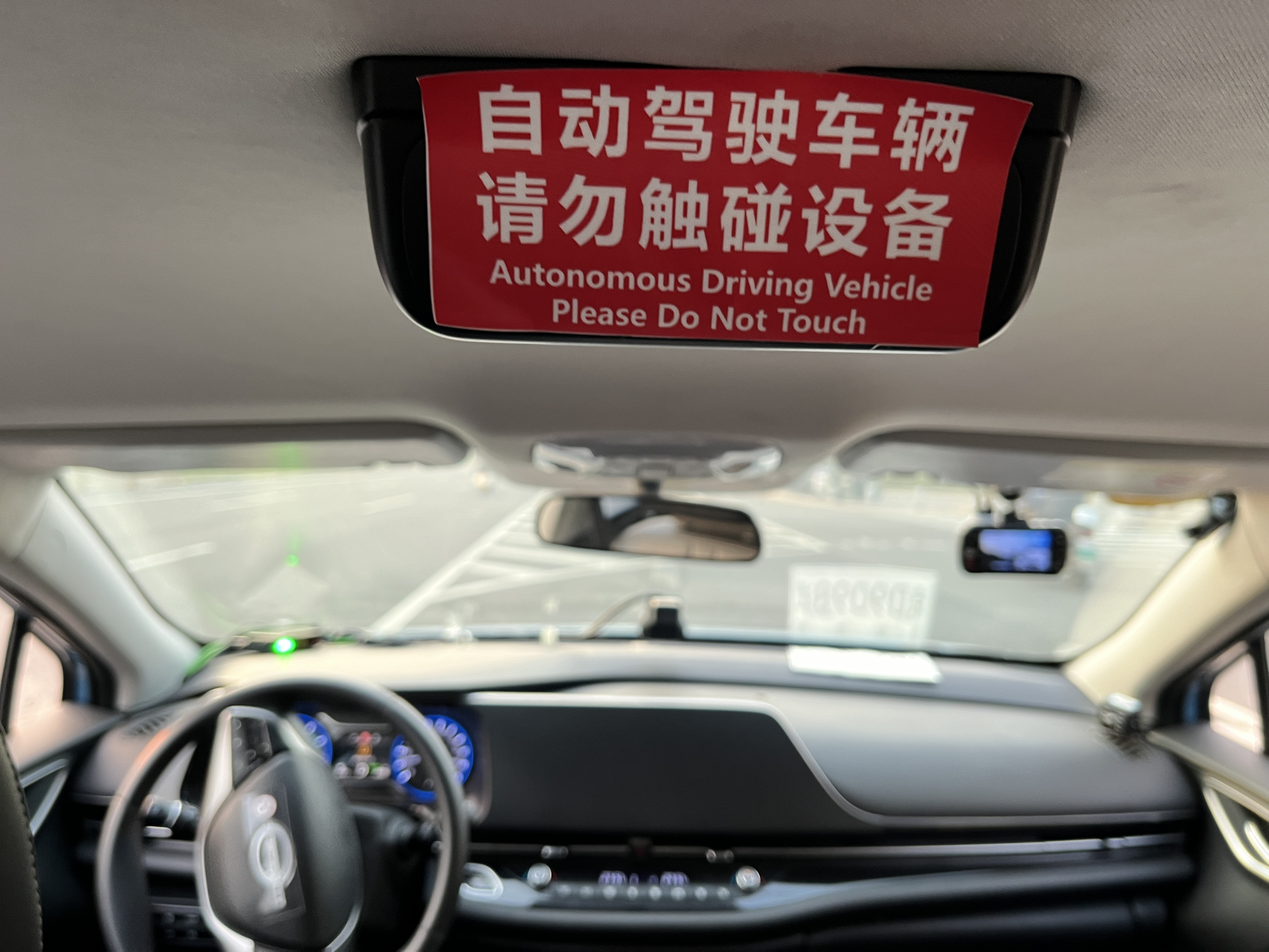 View from the back seat of an autonomous taxi. A sign says "Self-driving vehicle, please do not touch" in English and Mandarin.